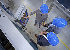 Overhead view of 3 staff members with blue hard hats discussing equipment in a factory
